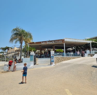 Lee Beach Food, Drinks & Cocktail Bar on a sunny day with patrons and palm trees.