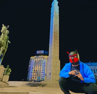 A man in a pup mask posing by a monument at night.