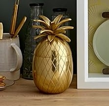 Gold pineapple ice bucket on a wooden shelf, decorative luxury home bar accessory.
