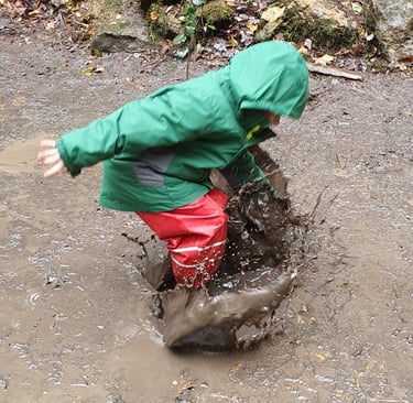 A child in waterproofs jumping into a muddy puddle and creating a splash.