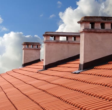 clay roof shingles with 3 white chimneys with a  blue sky background and clouds