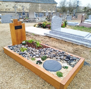Aménagement funéraire avec encadrement bois, galets gris, schiste et fleurs de saison.