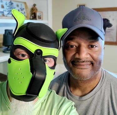 2 men, 1 wearing a pup mask, posing together.