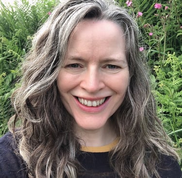 smiling woman with greying hair standing before wild flowers