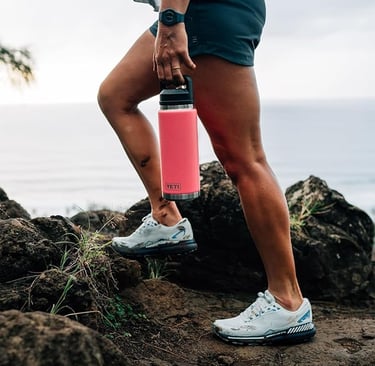 Pink YETI Rambler bottle filled with ice water at the beach.