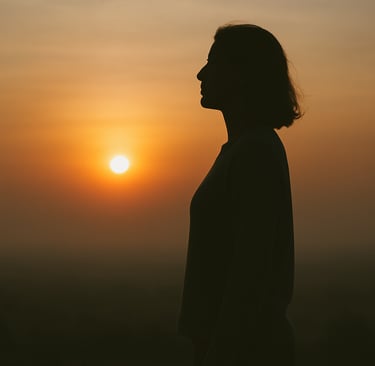 A silhouette of a woman standing quietly sunset—facing the light. A moment of calm and dignity.