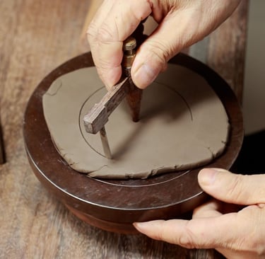 hand holding a wooden tool drawing circles on a clay slab