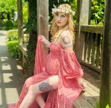 Pregnant woman in a crown and pink gown sitting on a wooden bench during maternity photoshoot—celebrating motherhood.