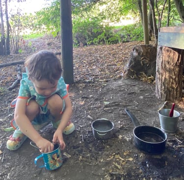 a young child in a woodland playing with a mud kitchen