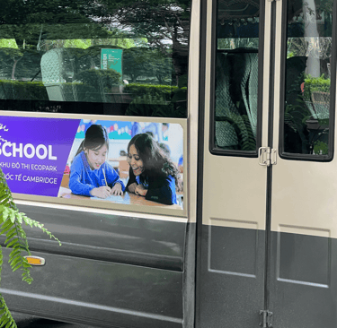 A bus with a advertisement of a school. The advertisement has a female teacher teaching students.