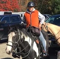 a woman in a vest and hat riding a horse