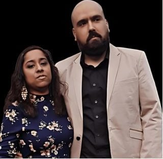 A well-dressed couple posing together, a man in a beige blazer and a woman in a floral dress.