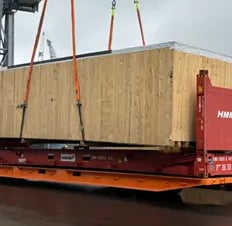 A red 40ft flat rack being loaded with a large wooden container