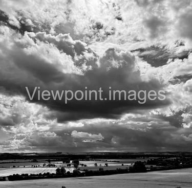 Dramatic black and white landscape of storm clouds over rural farmland and fields.