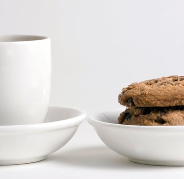a white cup of coffee and a white bowl of chocolate chip cookies.