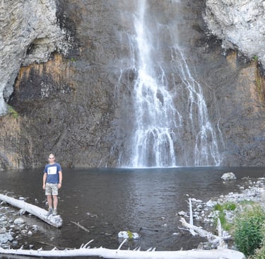 a man standing in front of Fairy Falls waterfall in Yellowstone National Park