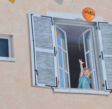 Détails d'une fenêtre en trompe-l'oeil peint sur une façade, un enfant avec ballons Ideklic, Jura 39