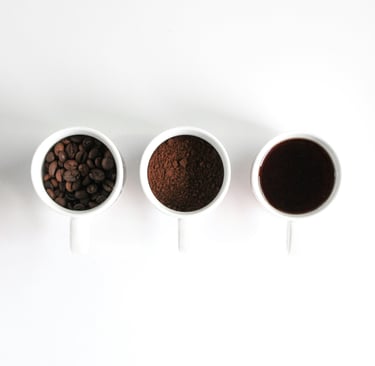 Three white cups in white background. one with coffee beans. one with coffee grinds. one with black coffee.