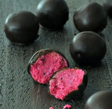 Several chocolate balls on a black countertop. One ball is split open, showing bright pink center