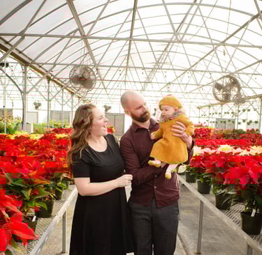 a man and woman holding a baby in a greenhouse