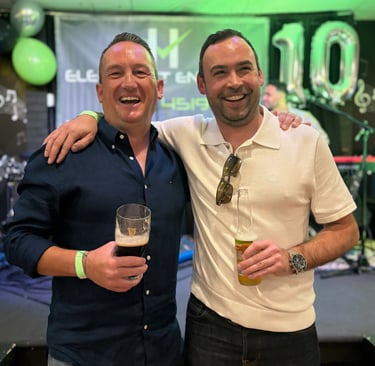 Two men standing together at a community event, holding drinks and smiling