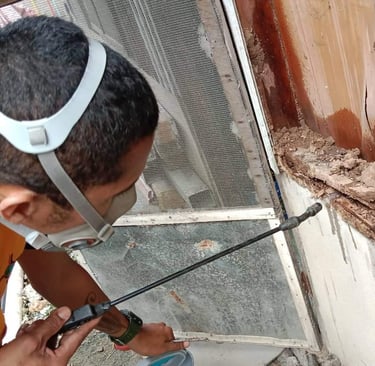 Pest control technician in a mask spraying a wooden door frame for termite damage and infestation.