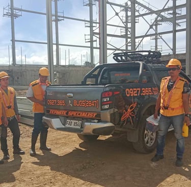 Termite specialist team in safety vests standing by a pest control truck at a construction site.