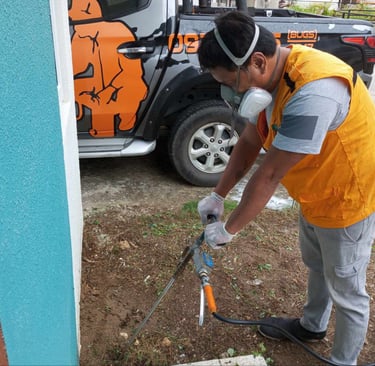 Professional pest control technician performing soil treatment for termite prevention near a home.