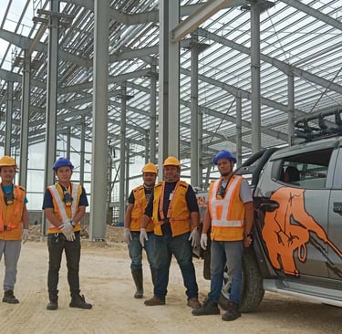 Termite control specialists in safety gear standing by a service truck at a commercial construction site.