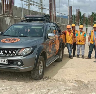 exterminators in safety gear standing by a Mitsubishi Triton pickup truck at a building site.