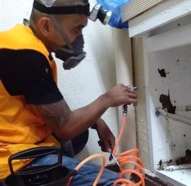 Professional termite control specialist treating wood damage in a kitchen cabinet with liquid termiticide.