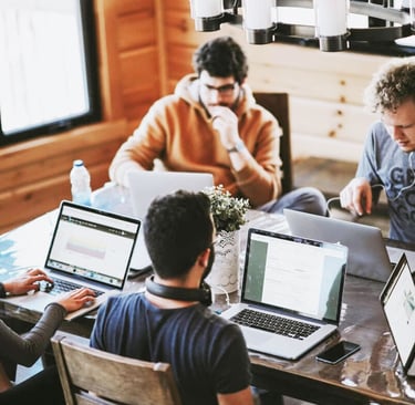 a group of people sitting around a table with laptops