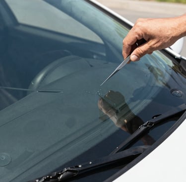 A friendly technician repairing a small windshield chip under bright Southern California sunlight.