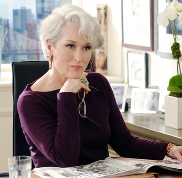 Miranda Priestly en su oficina con expresión analítica, representando el control y la exigencia en la industria de la moda
