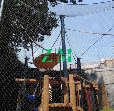 Outdoor adventure playground with wooden climbing frames, safety netting, and a tire swing.