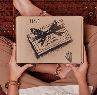 A person holding a 1 Hand cardboard gift box over a patterned rug, showing hand-drawn bow details.