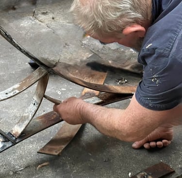 A skilled metalworker bends and shapes rusty metal strips for a custom sculpture project.