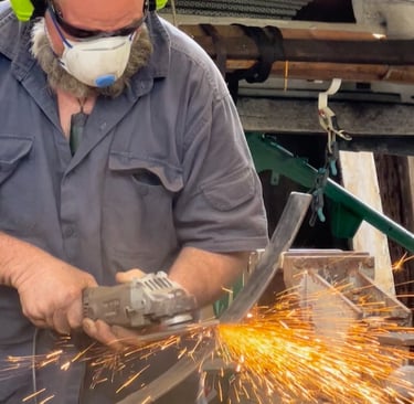 A metalworker wearing safety gear uses an angle grinder to cut metal, creating bright orange sparks.