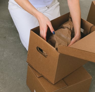 Moteris pakuojanti daiktus į dėžę persikraustant