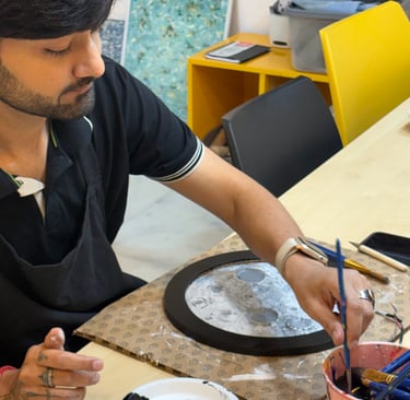 A male artist painting a circular moon lamp artwork using a brush and acrylic paints.