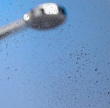 Water droplets on a shower glass panel with a blurred showerhead in an Auckland bathroom repaired by