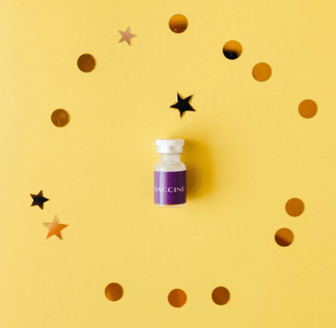 pequeño frasco de vacuna médica con etiqueta morada rodeado de confeti dorado