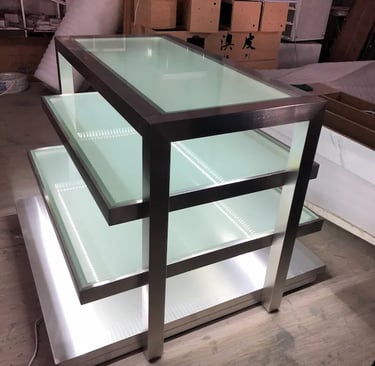 Modern 3-tier stainless steel display stand with illuminated frosted glass shelves for retail stores.