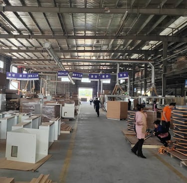 Workers assembling furniture in a large industrial woodworking factory warehouse.