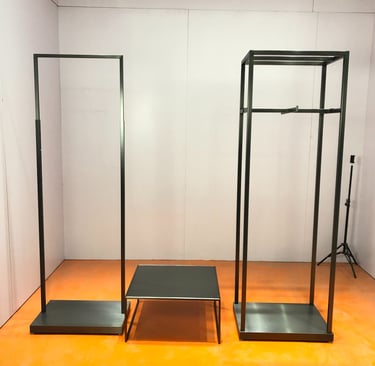Modern minimalist black metal clothing racks and display table set for a retail fashion boutique.
