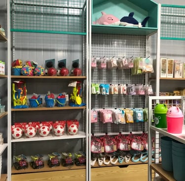 Retail store shelves displaying assorted children's toys, plush sharks, soccer balls, and colorful accessories.