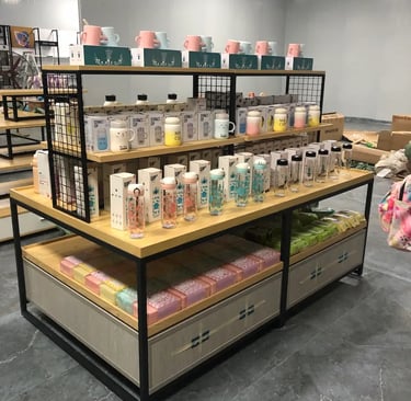 A retail display shelf featuring various ceramic mugs and glass water bottles in a modern gift shop.