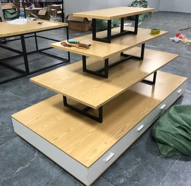 Four-tier wooden retail display table with black metal frames and white storage drawers.
