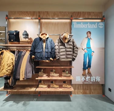 Timberland retail store display featuring winter jackets, beanies, and classic wheat work boots on shelves.