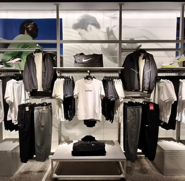 A Nike retail display featuring athletic apparel, workout shirts, jackets, and gym bags on metal racks.